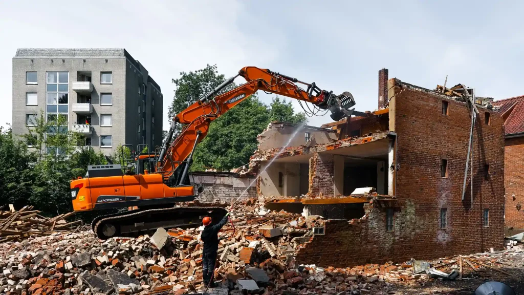 Orange excavator demolishing a brick building for a demolition contractor in Foothill Farms, CA