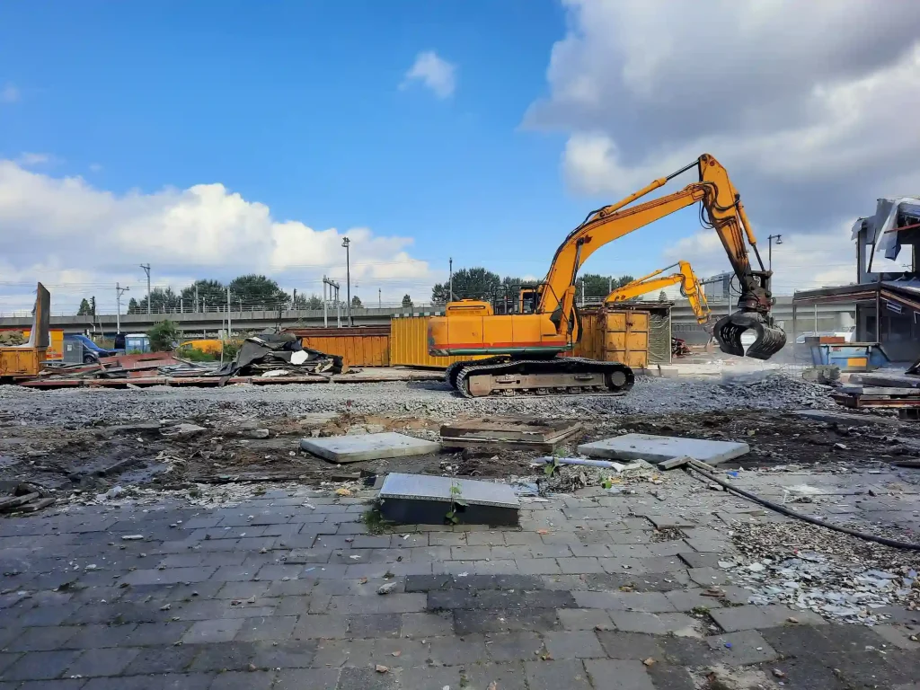 Excavator staged on a paved lot with rubble, showing planned truck routes and staging on a North Highlands, CA commercial job